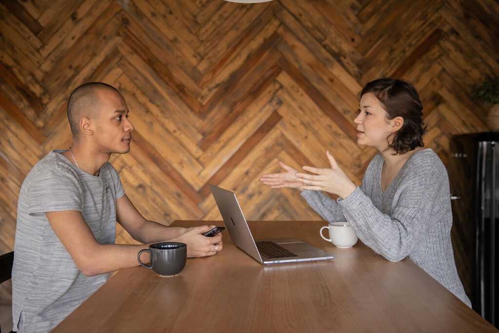 Two people sit at a table with a laptop out